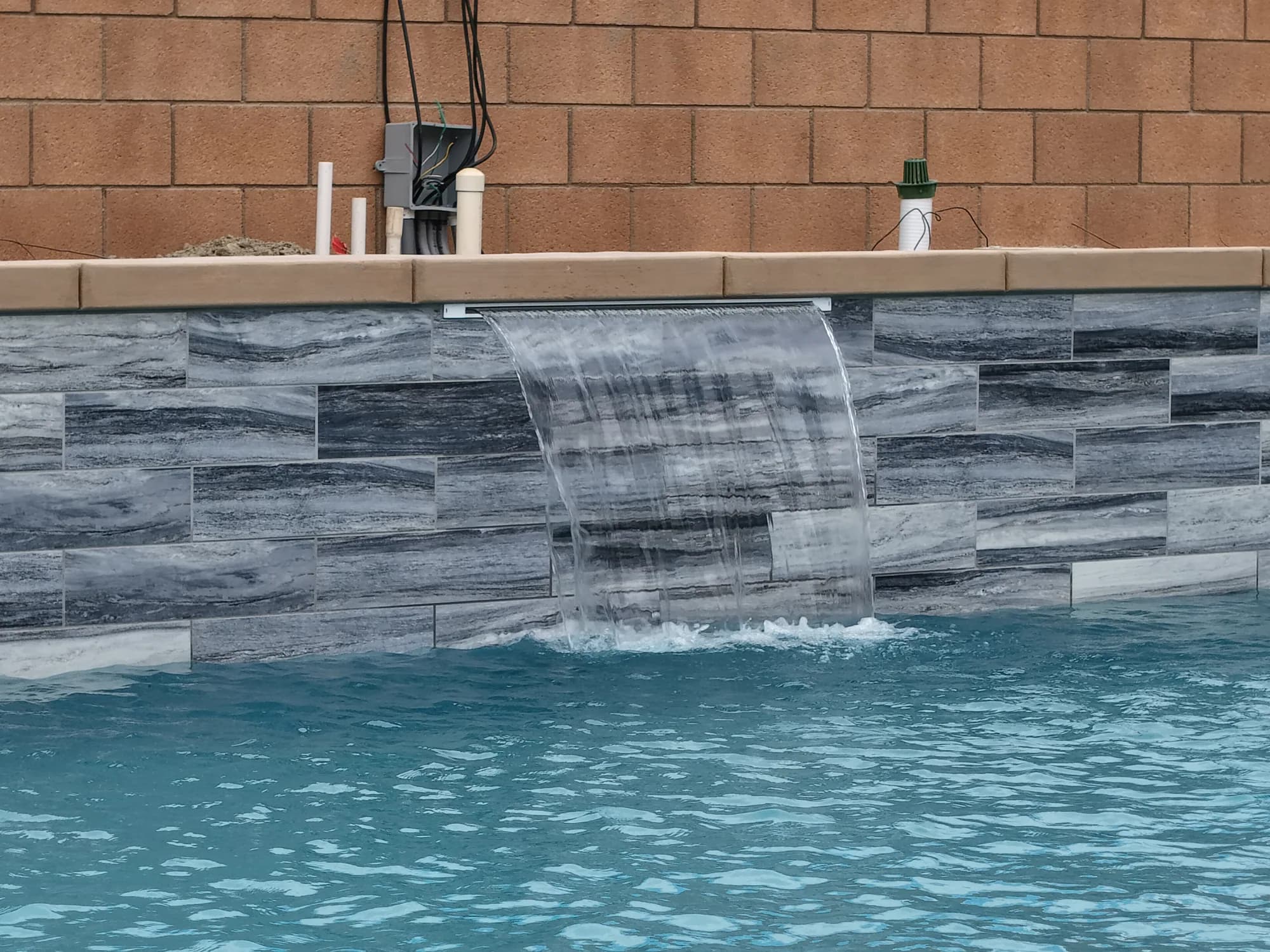 Stone-faced water wall and waterfall at the 56 AVE pool